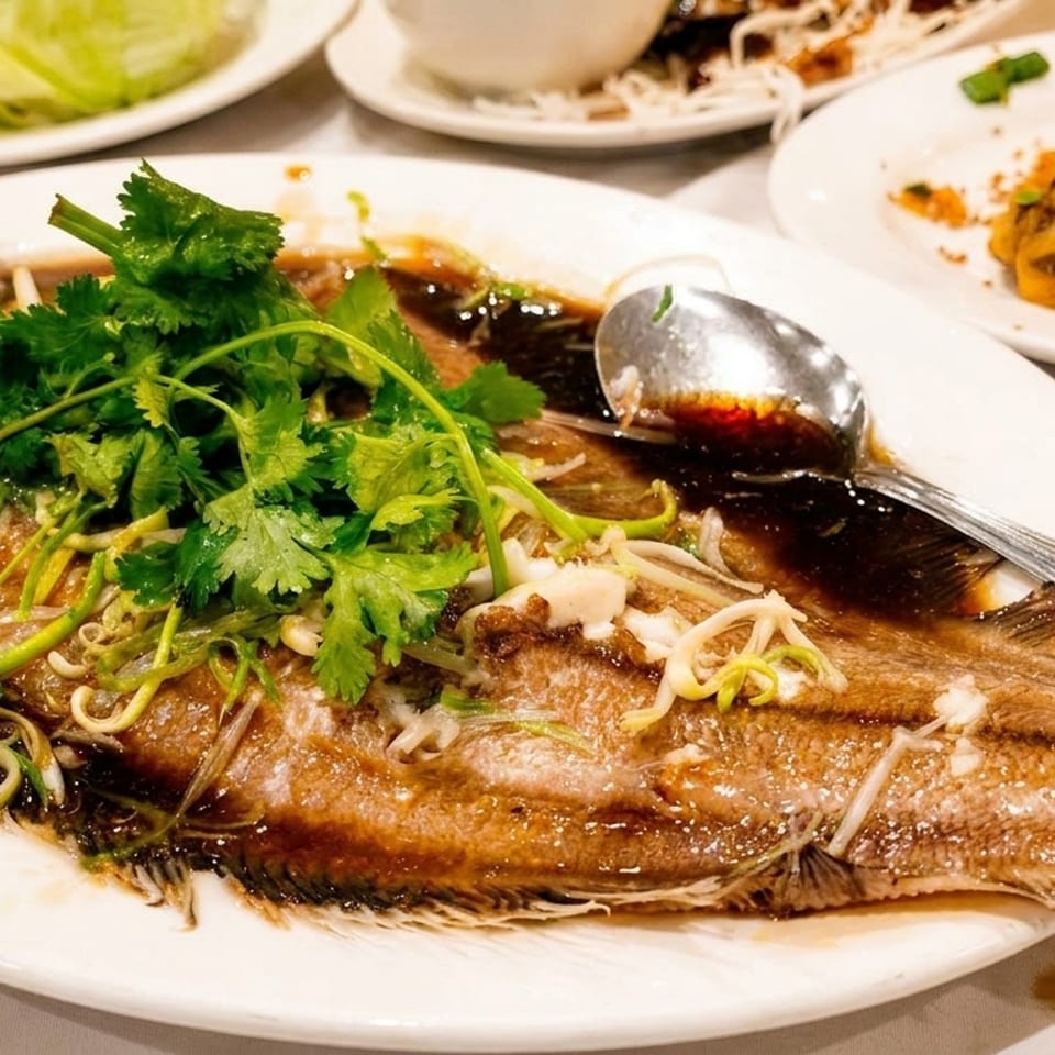 Steamed whole fish with dark sauce, fresh cilantro, and green onions on a white plate.