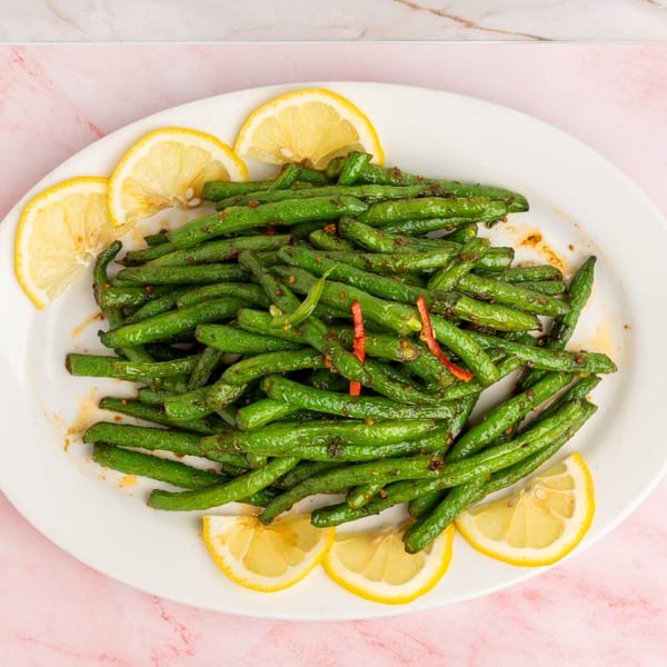 Sautéed green beans with red chili flakes and lemon slices on a white oval plate.