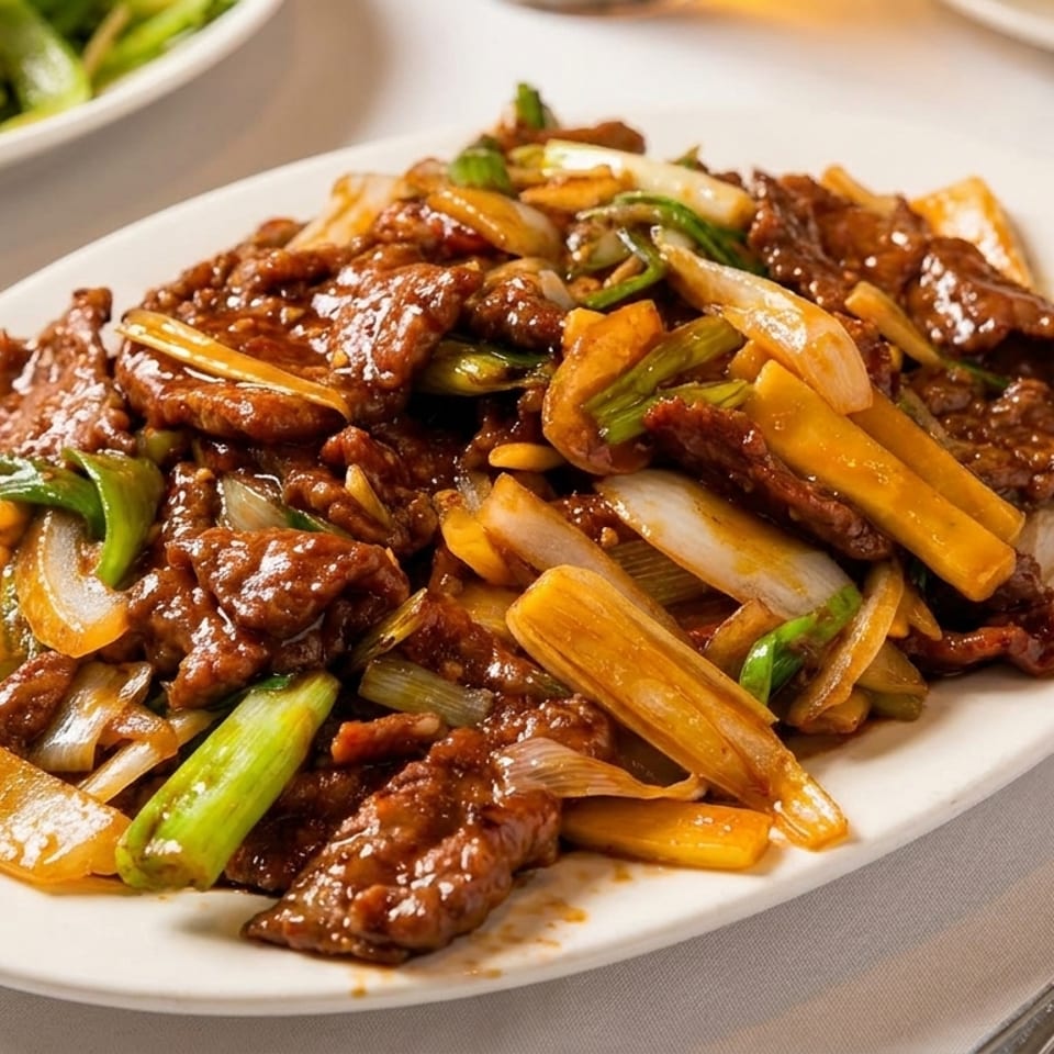 A white oval plate filled with beef stir-fry, green onions, and bamboo shoots on a white tablecloth.