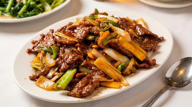 A white oval plate filled with beef stir-fry, green onions, and bamboo shoots on a white tablecloth.