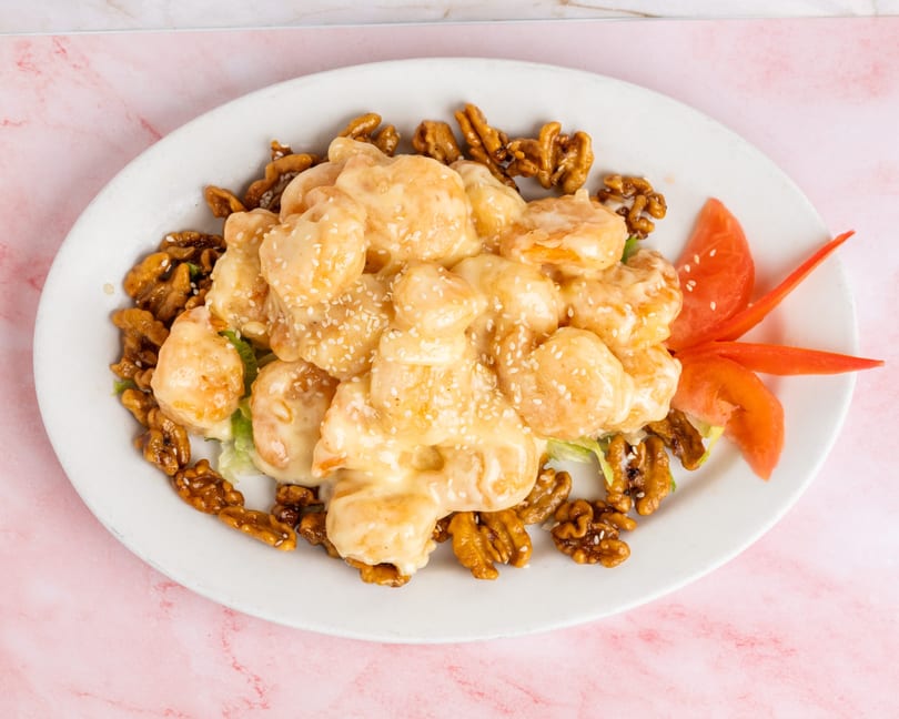 Honey walnut shrimp with sesame seeds, lettuce, and tomato on a white oval plate.