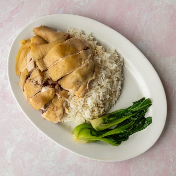 Hainanese chicken rice with sliced poached chicken, white rice, and green bok choy on a white plate.