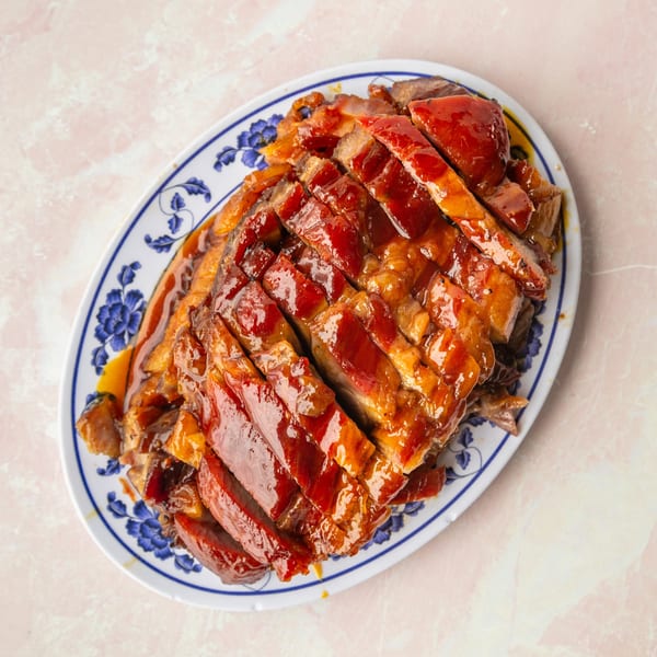 Sliced char siu (Chinese BBQ pork) with a glossy red glaze on a white and blue patterned platter.