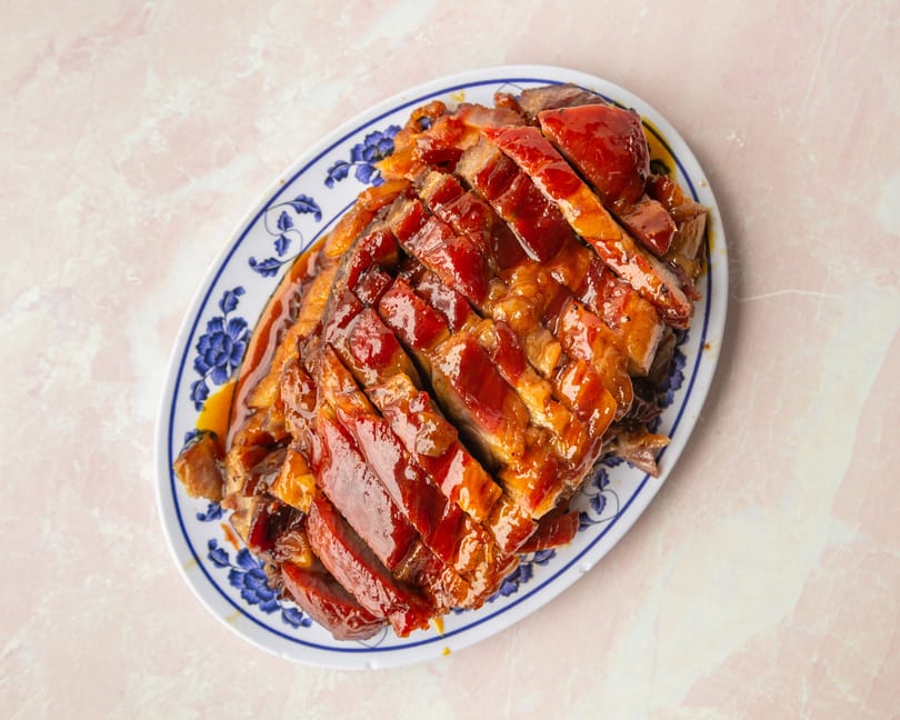 Sliced char siu (Chinese BBQ pork) with a glossy red glaze on a white and blue patterned platter.