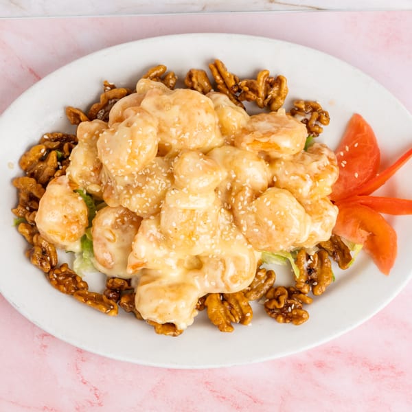 Honey walnut shrimp with sesame seeds, lettuce, and tomato on a white oval plate.