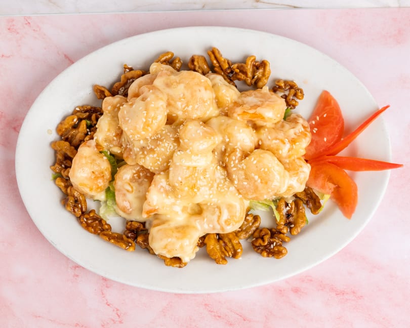 Honey walnut shrimp with sesame seeds, lettuce, and tomato on a white oval plate.