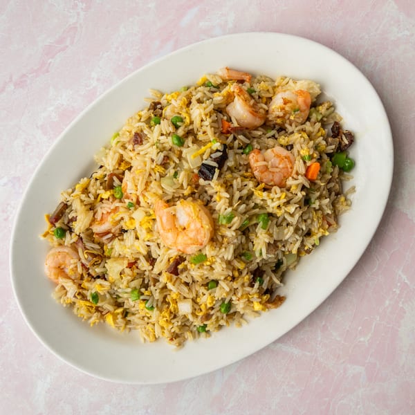 Shrimp fried rice with peas, carrots, and scrambled egg on a white oval plate.