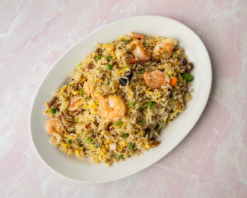 Shrimp fried rice with peas, carrots, and scrambled egg on a white oval plate.