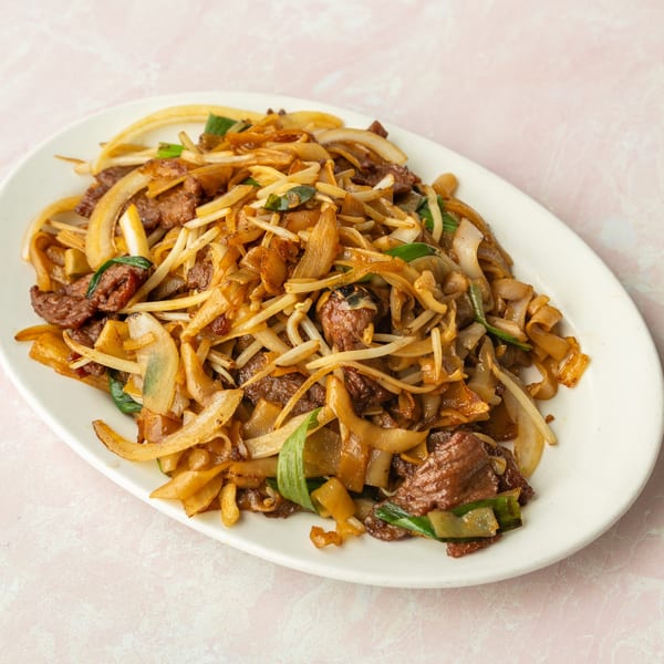 A white oval plate filled with beef chow fun, featuring wide noodles, beef, onions, and bean sprouts.