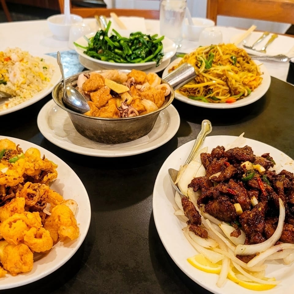 A round table laden with various Chinese dishes, including fried squid, noodles, and beef.