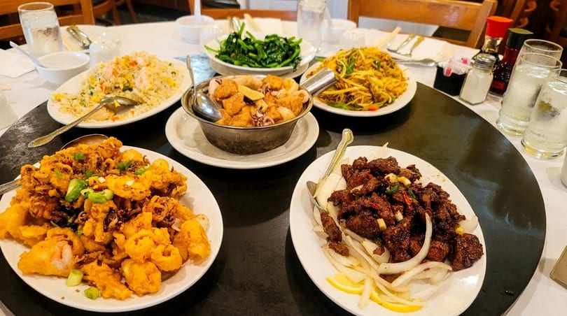 A round table laden with various Chinese dishes, including fried squid, noodles, and beef.